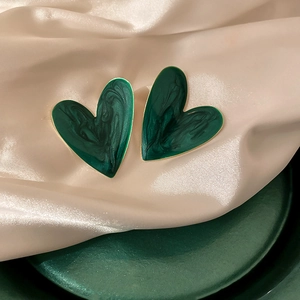Detail of dark green marble textured heart earrings with golden edges on silk fabric