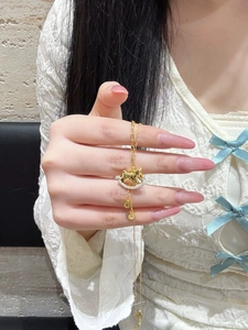 Golden rocking horse necklace detail with white zircon stones and tassel pendant on a hand