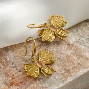 Gold butterfly earrings with textured wings and pink oval gemstones on silk fabric