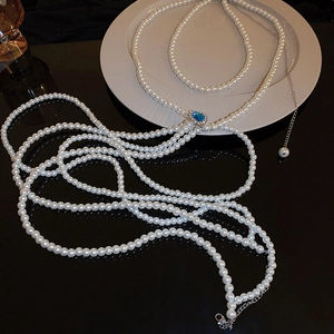 Detail of multilayer pearl body chain featuring a heart-shaped blue gemstone pendant