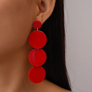 Detail of red acrylic tiered round drop earrings worn by a model in a close-up profile shot