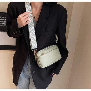 Detail view of light green PU crossbody bag with wide black and white woven strap