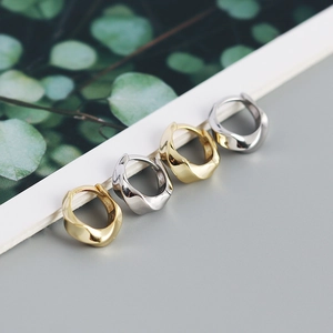 Macro shot of minimalist twisted geometric hoop earrings in polished gold and silver finish