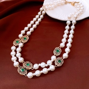 Close-up of vintage double-layer pearl necklace with green gems on red silk background