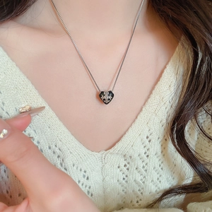 Detailaufnahme einer schwarzen Herz-Halskette mit Silberkreuz an einem Model