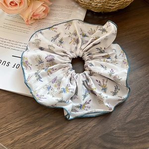 Detailed view of floral satin scrunchie with blue edges on a rustic wooden table