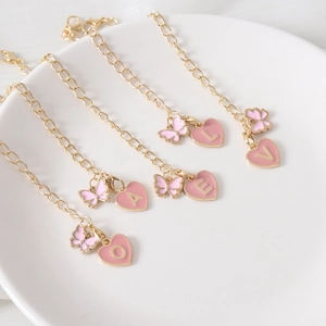 Gold-tone butterfly charm bracelets with pink enamel heart letters on a white plate