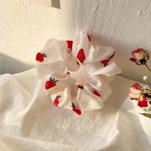 Detail of white scrunchie with red strawberry print on white fabric with dried roses