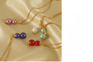 Detail of five multi-color gourd pearl pendants on gold stainless steel chains over silk