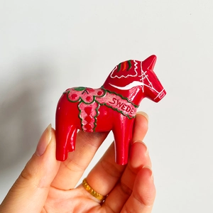 Close-up of a hand-held red wooden Dala Horse magnet with Sweden text engraving