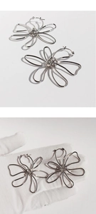 Macro shot of silver oversized floral earrings shown in palm to demonstrate large scale