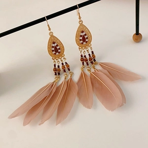 Macro view of bohemian drop earrings featuring intricate beads and light pink feathers