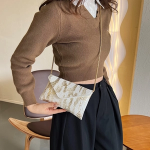 White faux crocodile skin envelope bag with golden chain strap worn by a female model