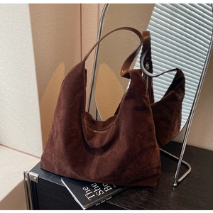 Close-up of a large brown suede Hobo bag with decorative stitching on a black cabinet