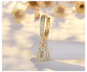 Close-up of a gold earring with micro-paved letter D pendant on a white pebble
