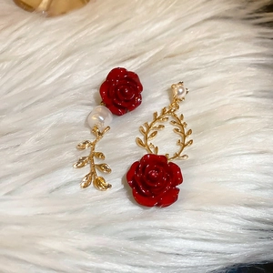 Detailed view of asymmetric red rose and pearl earrings with golden leaf accents