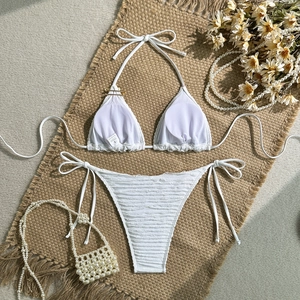Flat lay of white textured bikini with ties, pearls, and daisies on a rustic burlap mat
