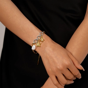 Detail of nautical charm bracelet with baroque pearl and golden starfish on wrist
