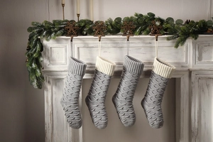 Detail of four grey knitted Christmas stockings with fish scale texture on white fireplace
