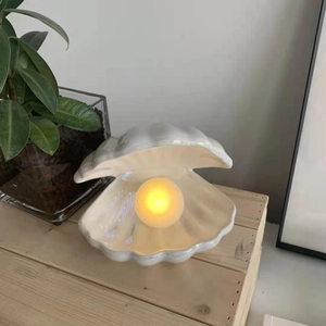 Detailed view of ceramic shell lamp with warm glowing pearl on a wooden base