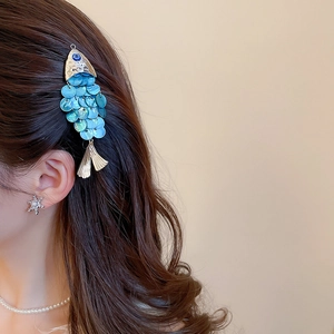 Detailed view of a golden fish-shaped hair clip with blue scales worn on dark brown hair