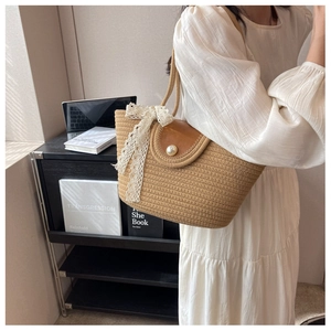 Detail of straw tote bag with brown leather flap, pearl buckle and white lace ribbon