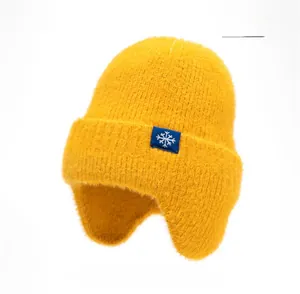 Vue détaillée d'un bonnet tricoté jaune avec cache-oreilles et étiquette de flocon bleu