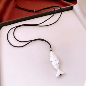 Detailed view of silver fish pendant with scale textures on black woven cord necklace