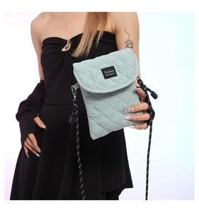 Detail of light green quilted crossbody bag with adjustable black and white woven strap
