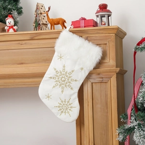 Detailed view of white plush Christmas stocking with gold snowflake embroidery on a fireplace
