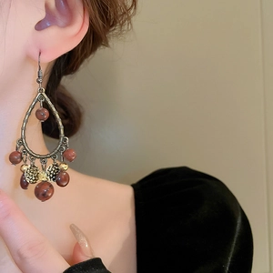 Ethnic style teardrop earrings with bronze metal and reddish-brown beads on a model
