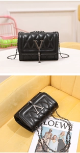 Close-up of black quilted leather crossbody bag featuring V-shaped buckle and fringe detail