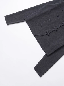 Detail of dark grey knit top showing decorative round buttons and waist knot accents