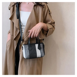 Detail of striped canvas handbag with black handles and gold hardware on a trench coat