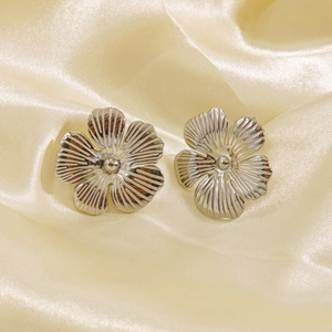 Minimalist silver flower stud earrings in textured stainless steel on beige silk fabric