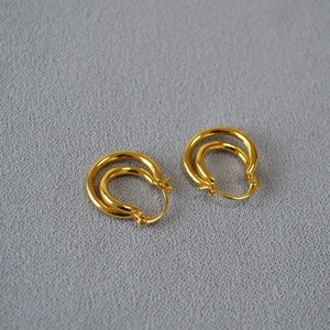 Minimalist double-hoop gold-plated brass twisted earrings on grey fabric background