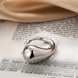 Macro view of polished silver water drop ring on vintage book and silk fabric