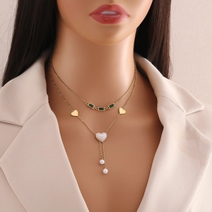 Double-layered gold necklace featuring emerald green stones and heart-shaped pendant