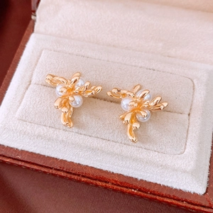 Macro shot of gold coral floral earrings with white pearls on a soft velvet jewelry box