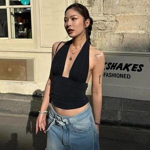 Detail of a black halter neck deep V-neck top with pleated texture on a model outdoors