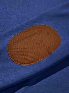 Detailed macro view of blue knitted fabric with a brown oval elbow patch and stitching
