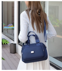 Detailed side view of navy blue nylon crossbody bag on model in modern outdoor setting