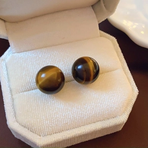 Macro shot of tiger eye stone ball earrings in a white velvet jewelry box display