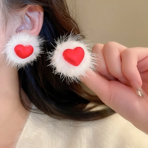Detail of soft white fur ball stud earring with red heart center worn on a model ear