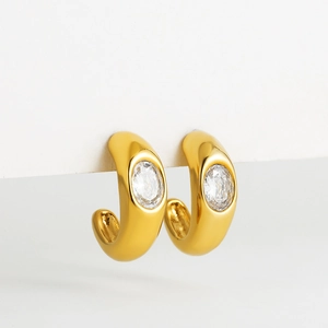 Detailed close-up of chunky gold C-shape earrings with inlaid oval zircon on a white display