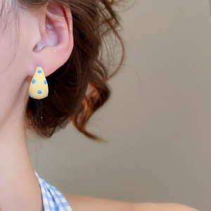 Close-up of yellow teardrop earring with blue dots worn on a model's ear