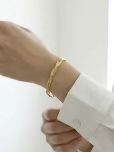 Detail of elegant twisted snake chain bracelet on wrist showing a refined gold-plated texture