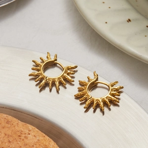 Boucles d'oreilles soleil dorées avec texture de lave irrégulière sur plateau en métal