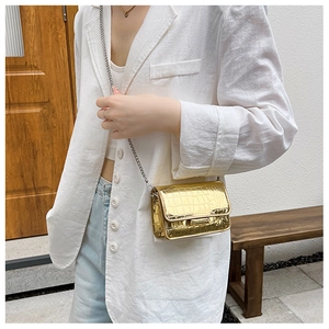 Close-up of mini gold crossbody bag with crocodile texture and silver chain strap
