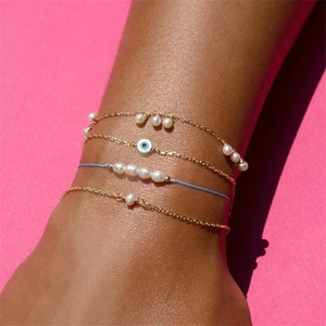 Detail of layered gold bracelets with white pearls and blue evil eye charm on wrist